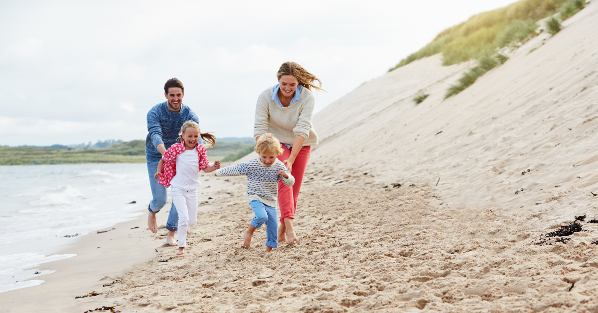 two parents and 2 children running on the beach